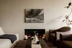 A minimalist living room featuring a wooden fireplace with lit candles, a vase with flowers, and a dark wooden coffee table.