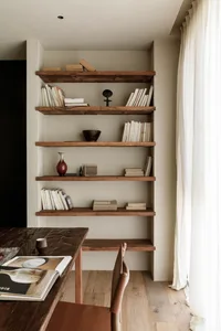 A minimalist living room featuring wooden shelves with various books and decorative items.
