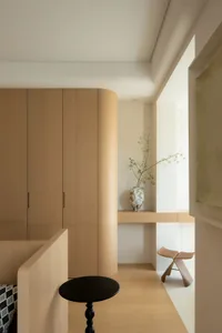 A modern minimalist bedroom with wooden furniture, a black side table, and a vase with green plants on a shelf.