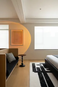 A minimalist bedroom featuring a sleek black platform bed, a black and white geometric rug, a wooden bench with a black and w