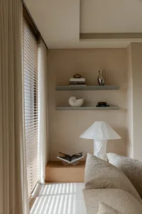 A minimalist interior featuring a comfortable sofa by a window with curtains and a bookshelf.