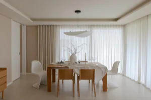 A minimalist dining room with white wooden furniture and white linen curtains.