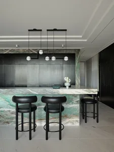 Modern bar counter made of marble with black bar stools and pendant lights.