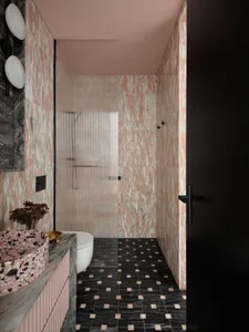 A modern bathroom with pink marble tiles and a black floor.