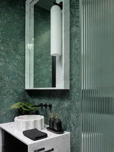A modern bathroom with green marble walls and white marble countertop, featuring a black faucet and a black and gold soap dis
