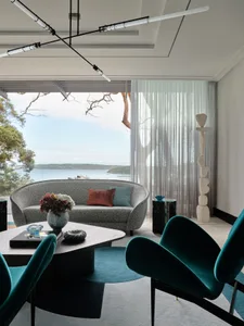 A modern living room features a gray fabric sofa with blue and brown cushions, green velvet armchairs, a coffee table, and a 