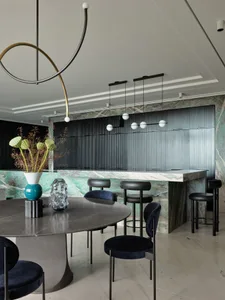 A modern dining room featuring a round marble table surrounded by black chairs and stools, with a green marble backsplash and