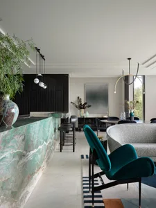 Modern living room with a marble counter, green upholstered chair, and glass dining table.
