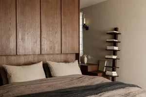 Modern minimalist bedroom featuring a brown bed with wooden headboard, shelves, and books.