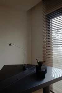 A minimalist office space featuring a black wooden desk with a modern metal lamp and decorative metal bird.