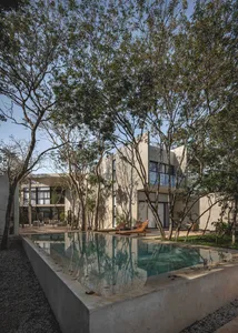 A modern residential pool house with concrete walls and bamboo accents, featuring a large outdoor swimming pool surrounded by