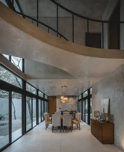 A modern residential dining room with concrete flooring, stone walls, and large windows overlooking an outdoor area.