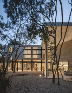 A modern residential interior with concrete walls and floors, featuring a spacious living room and a well-lit dining area.