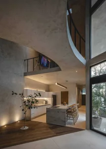 Modern residential kitchen featuring a concrete island with a cooking area, white cabinetry, and a dining table with wooden c