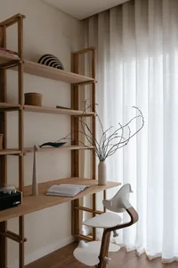 A modern work station with wooden materials, featuring a bookshelf, a desk, and a white chair in front of a large window with