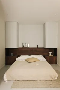 A minimalist bedroom featuring a comfortable bed with a textured fabric cover, two side tables, and integrated storage soluti