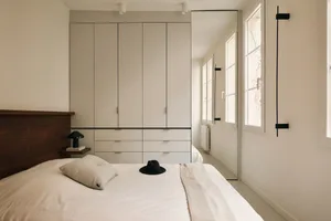 A minimalist bedroom with a white fabric bed, light wood furniture, and metallic accents.