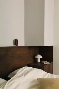 A minimalist bedroom featuring a wooden headboard, ceramic side table, and fabric bedding.