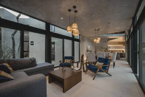Minimalist living room with concrete flooring and furniture, modern pendant lights, and large windows.