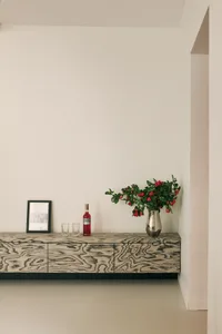 A modern interior design featuring a wooden console table with metal accents, accompanied by a vase of roses, glasses, and a 