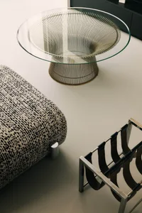 A minimalist glass side table with a metal base sits on a plain surface.