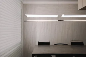 A minimalist office space with a concrete and wooden table and chairs, featuring modern lighting and a concrete wall.