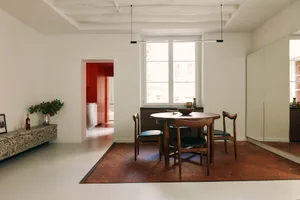 A modern dining room with a round wooden table, black chairs, and a hanging light fixture.