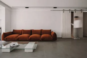 A modern living room featuring a large, plush couch with brown upholstery on a concrete floor.