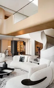 A modern living room featuring sleek, white furniture, a spiral staircase, and a wine cabinet with amber lighting.