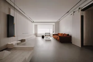 A minimalist residential interior featuring a concrete floor and walls, with a long, low-slung sofa in a warm orange hue.