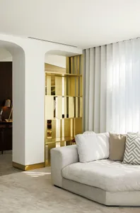A minimalist living room featuring a gold metallic shelving unit and a comfortable neutral-colored sofa.