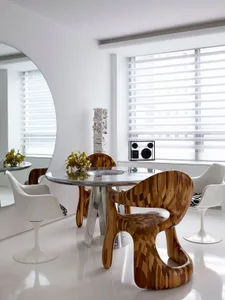 Modern dining room featuring a round wooden table and decorative wooden chairs surrounded by white furniture.
