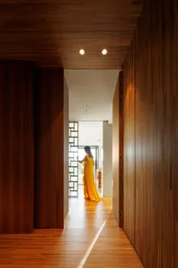 A modern hallway with wooden walls and floors, featuring a woman in a yellow dress standing near a glass partition.