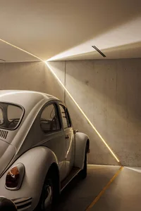 A white Volkswagen Beetle parked in a modern, minimalist concrete car parking space with linear lighting.