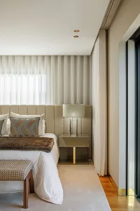 Modern minimalist bedroom featuring a bed with white linens, patterned pillows, and a textured headboard, illuminated by a la