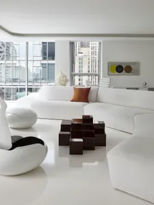 Modern, minimalist white lounge area with fabric seating and geometric coffee table, overlooking urban cityscape.