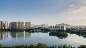 A serene cityscape view featuring tall glass buildings, concrete skyscrapers, and lush greenery surrounding a calm lake.