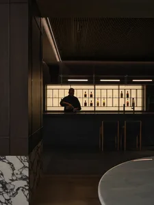 A dark-wood and marble industrial-style restaurant bar with a bartender preparing drinks.