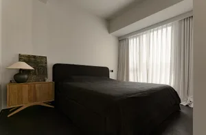 Bedroom featuring minimalist design with black textiles and white wooden furniture.