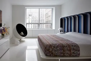 A minimalist bedroom featuring a modern bed with a colorful striped headboard and a sleek, white floor and furniture.