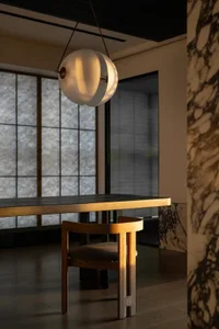 A minimalist interior design featuring a wooden chair, marble table, and metal pendant light.