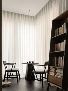 A minimalist residential space featuring wood and glass materials, with a small table and chairs, and a bookshelf.