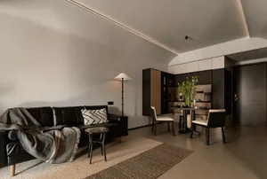 Modern living room featuring a black leather sofa with a blanket, contemporary floor lamp, and wooden dining table with chair