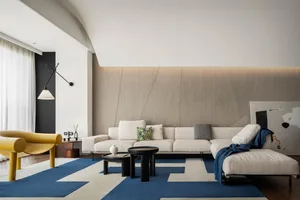 A modern living room featuring a white sectional sofa with a geometric blue and white rug, black coffee tables, and a yellow 