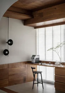 Modern home office with a walnut desk and minimalist design, featuring a black wall lamp and a window with blinds.