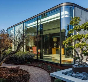 Modern glass building exterior with curved windows and landscaping.