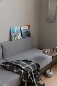 A minimalist living room featuring a modern grey couch adorned with a checkered blanket, accompanied by a small side table wi