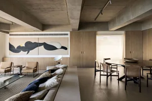 A modern minimalist living room with a concrete ceiling, wooden furniture, and large abstract painting.