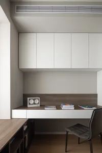 Modern study area featuring a white desk, dark wood floor, and white cabinets.