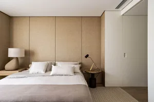 A minimalist bedroom with neutral-toned walls, bed, and bedding, featuring simple and functional design elements.